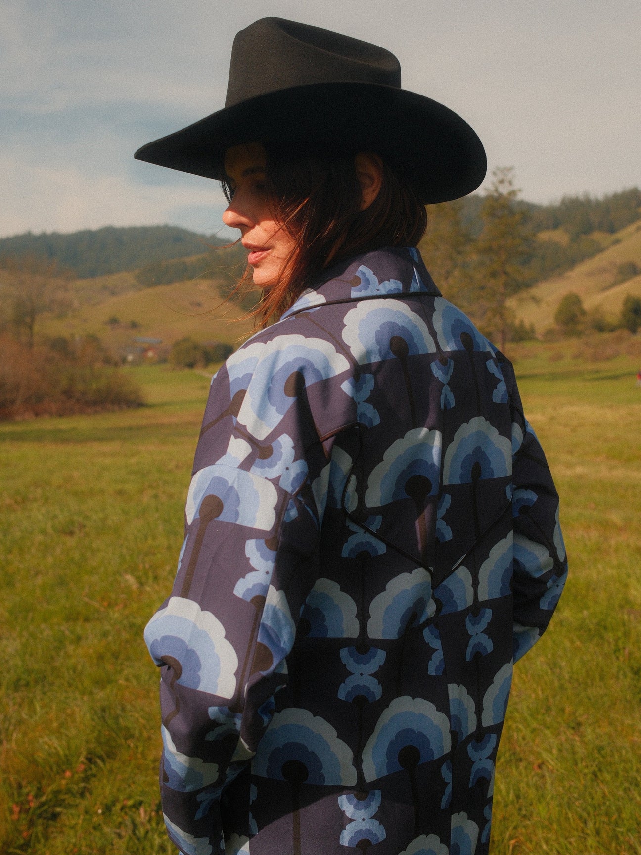 Back view showing the dropped shoulders, in a meadow, Midnight Plumes brushed cotton car coat